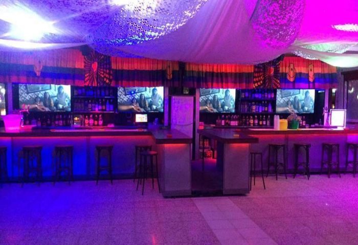 Coco Loco Gay Bar in Gran Canaria. Interior view, bar with stools, TV screens, bottles, purple and red lighting. Gay travel advice.