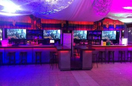 Coco Loco Gay Bar in Gran Canaria. Interior view, bar with stools, TV screens, bottles, purple and red lighting. Gay travel advice.