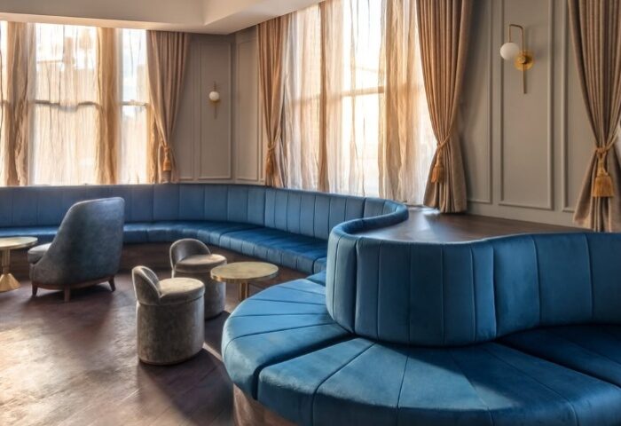 Sydney's Colombian Hotel lounge area. Blue velvet seating, small tables, and large windows with sheer curtains. Gay travel advice.