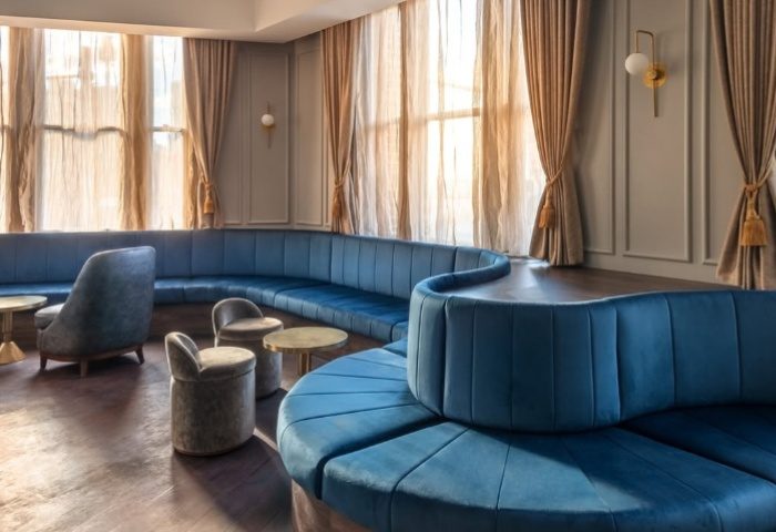 Sydney's Colombian Hotel lounge area. Blue velvet seating, small tables, and large windows with sheer curtains. Gay travel advice.