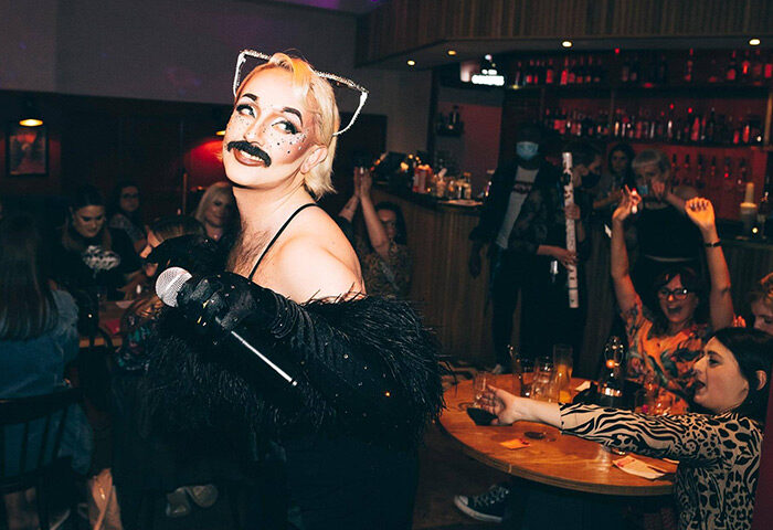 Drag show at Colours Hoxton, Shoreditch, London. Performer with a mustache and cat ears sings to an appreciative crowd at the nightclub.