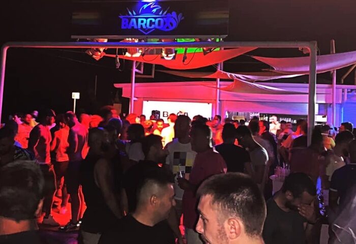 Night scene at Company Club Milano, a gay bar. Crowd of men under colorful lights, enjoying the outdoor party atmosphere. Gay travel advice.