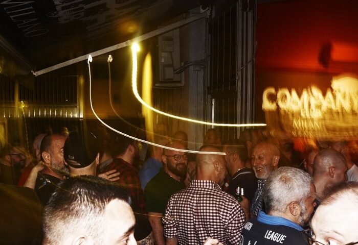 Company Club Milano crowd scene. Gay bar nightlife in Italy. Men socializing, blurred lights, and a lively atmosphere. Gay travel advice.