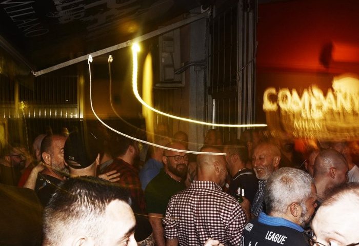 Company Club Milano crowd scene. Gay bar nightlife in Italy. Men socializing, blurred lights, and a lively atmosphere. Gay travel advice.