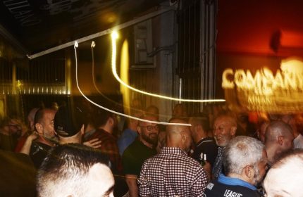 Company Club Milano crowd scene. Gay bar nightlife in Italy. Men socializing, blurred lights, and a lively atmosphere. Gay travel advice.