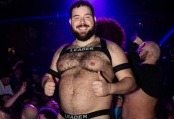 Gay Rome: A smiling, hairy man in a harness and underwear labeled LEADER gives two thumbs up at a gay club in Rome, Italy.