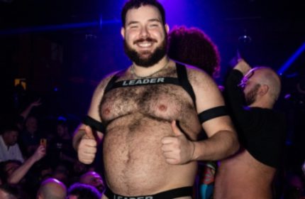 Gay Rome: A smiling, hairy man in a harness and underwear labeled LEADER gives two thumbs up at a gay club in Rome, Italy.