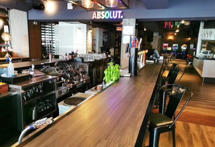 Complexe Sky bar interior in Montreal. Long wooden bar with stools, liquor bottles, and an Absolut neon sign. Gay bar travel advice.