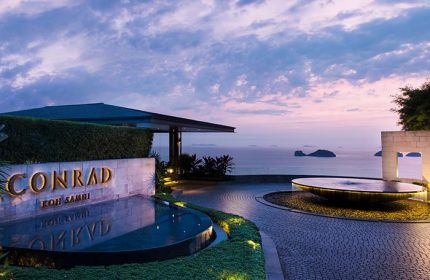 Entrance to Conrad Koh Samui luxury resort. A gay travel destination with ocean views, water features, and tropical landscaping at sunset.