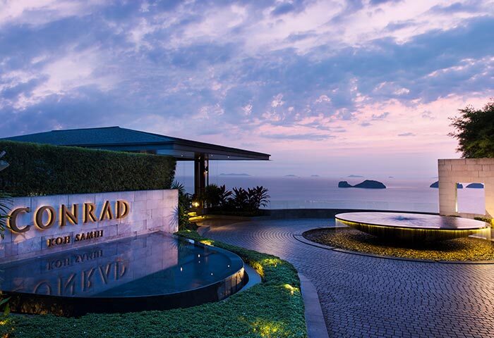 Entrance to Conrad Koh Samui luxury resort. A gay travel destination with ocean views, water features, and tropical landscaping at sunset.