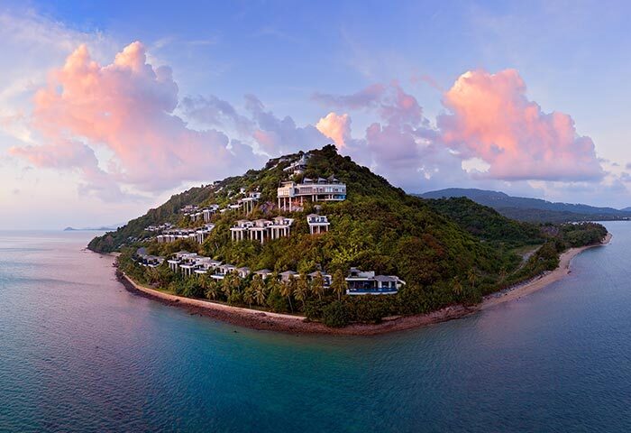Conrad Koh Samui aerial view. Villas dot a lush, tropical hillside meeting turquoise waters. A gay travel paradise in Thailand.