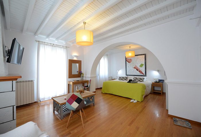 Elena Hotel Mykonos Town room. Cool design, cheap price gay hotel. Bedroom with archway, wooden floors, desk, and colorful chair.