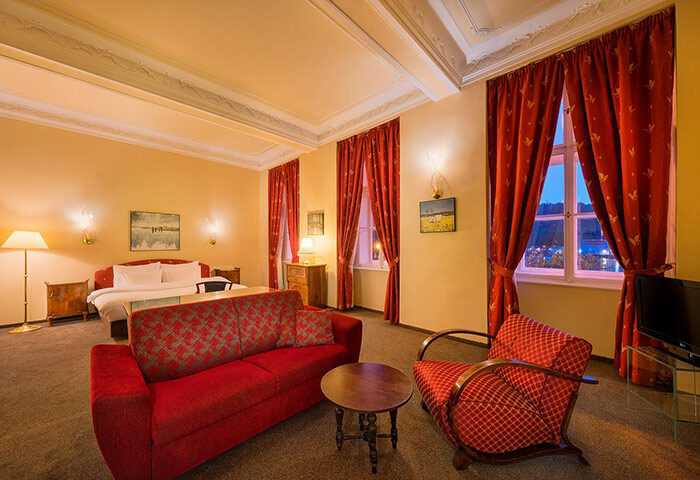 Hotel Leonardo Prague suite. Cool design gay hotel in Prague Old Town city center. Red sofa, chair, bed, & curtains.