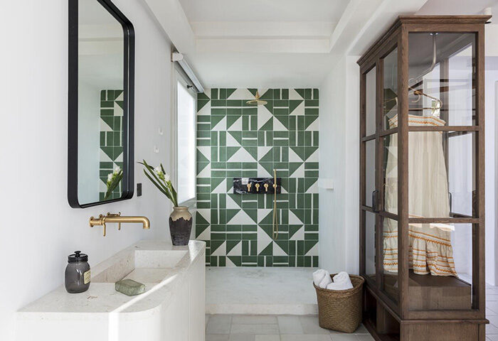 Upscale Porto Mykonos Hotel bathroom. Cool design with green geometric tiles, stone sink, and glass wardrobe. Gay hotel in Mykonos Town.