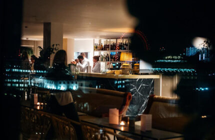 Assembly Hotel, London: Cool, cheap, gay-friendly hotel bar at night. Bartenders serve drinks. City skyline view. Travel advice for gay men.