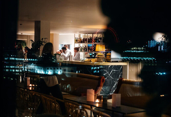 Assembly Hotel, London: Cool, cheap, gay-friendly hotel bar at night. Bartenders serve drinks. City skyline view. Travel advice for gay men.