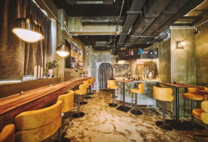 Interior of Fa Gai, a cool gay cocktail bar in Hong Kong. Features a long wooden bar, yellow stools, and industrial-chic design. Gay travel guide.