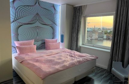 Nhow Berlin hotel room with river view. Coolest gay hotel in Berlin. Pink bedding, modern design, and city skyline. Gay travel.