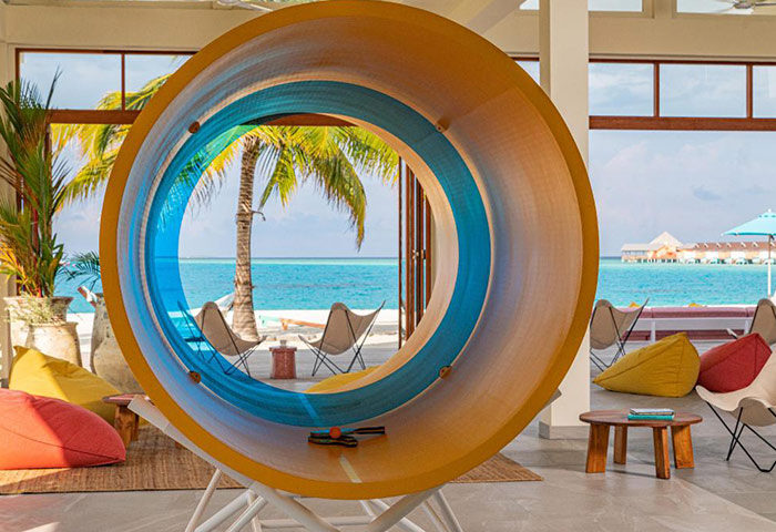 The Standard, Huruvalhi Maldives: Circular structure framing ocean view. Coolest gay hotels. Beach, palm trees, and lounge seating visible.