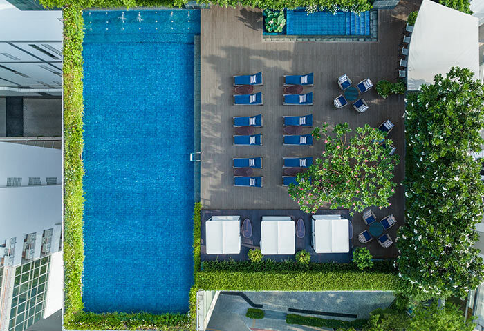 Le Méridien Bangkok rooftop pool aerial view. Loungers, cabanas, and lush greenery surround the pool. Coolest gay hotel in Bangkok.