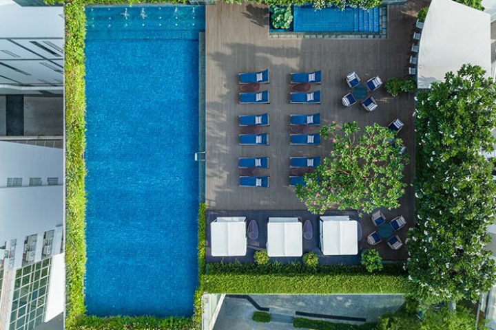Le Méridien Bangkok rooftop pool aerial view. Loungers, cabanas, and lush greenery surround the pool. Coolest gay hotel in Bangkok.