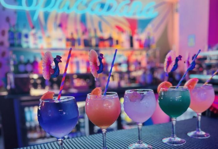 Colorful cocktails at Copacabana Gay Bar in Gran Canaria. Drinks with peacock garnish, straws, and orange slices on a bar top. Nightlife.