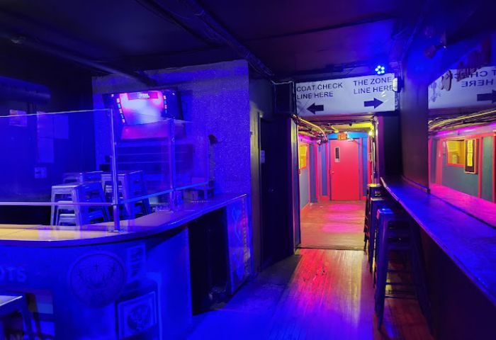 Interior of Crews & Tangos gay bar, Toronto. Hallway with bar, coat check sign, and colorful lighting. Gay travel advice.