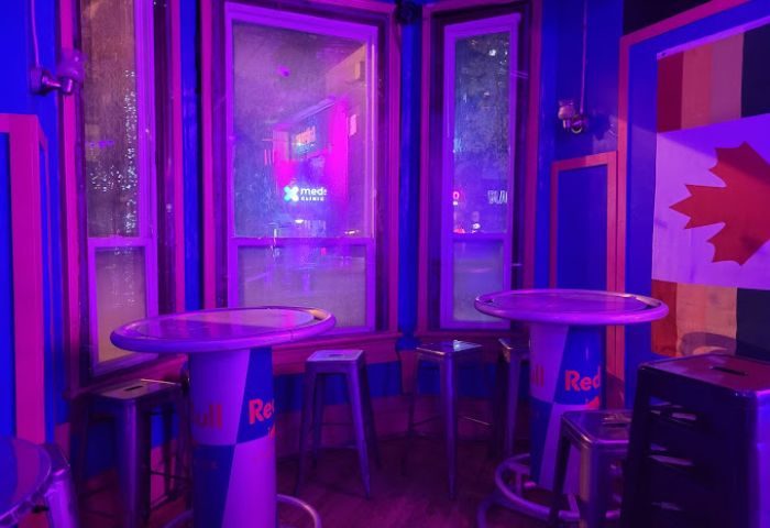 Interior of Crews & Tangos, a gay bar in Toronto. Canadian & Pride flags, tables made from Red Bull cans, & purple lighting.