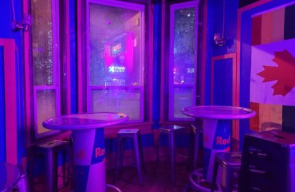 Interior of Crews & Tangos, a gay bar in Toronto. Canadian & Pride flags, tables made from Red Bull cans, & purple lighting.