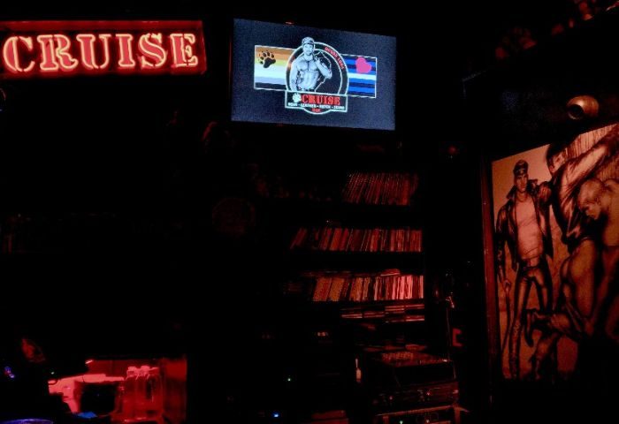 Cruise Bar Gran Canaria: Dark interior of the gay cruise club, with neon sign, TV screen, and artwork featuring muscular men.