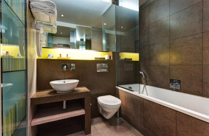 Hotel Elixir, a stylish gay hotel in Paris, features a modern bathroom. It includes a sink, toilet, bathtub, and brown tile design.