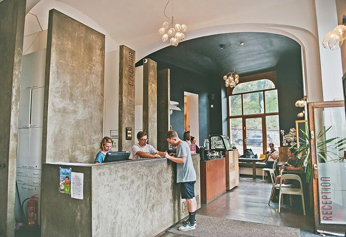 Czech Inn Prague hostel reception. Modern design, concrete desk, staff assisting guest. Gay-friendly accommodation in Vinohrady gayborhood.
