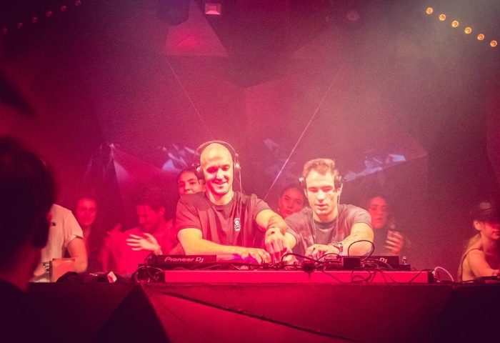 D9-Dark-Nine Budapest: Two DJs performing at a gay club in Budapest, bathed in red light, creating an energetic atmosphere. Gay travel advice.