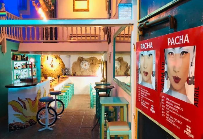 Dado Bar, a gay bar in Ibiza. Colorful interior with bar stools, tables, and Pacha posters. A great spot for drinks and nightlife.