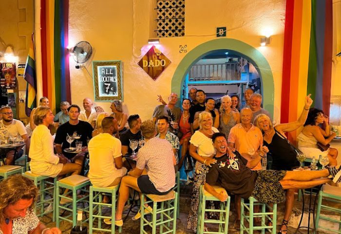 Dado Bar, gay bar in Ibiza. People enjoying drinks, rainbow flag, and vibrant nightlife. Gay travel destination.