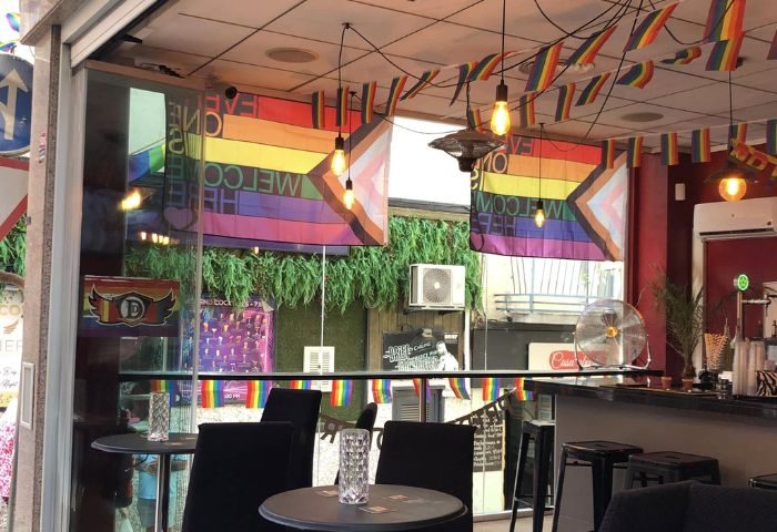 Interior of DD's Bar, a gay bar in Benidorm. Rainbow flags, tables and chairs visible. Gay travel destination.