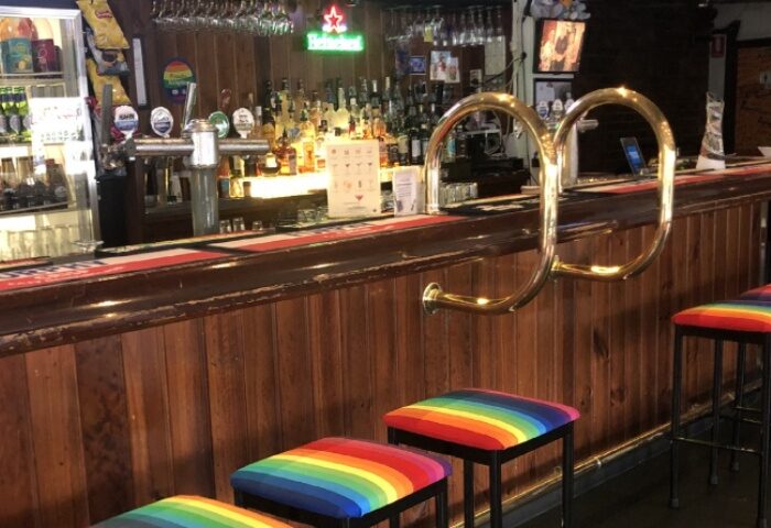 Richmond Hotel bar with rainbow stools. Gay travel advice for a welcoming gay bar in Melbourne. Drinks, bar stools, and wood paneling.