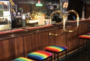 Richmond Hotel bar with rainbow stools. Gay travel advice for a welcoming gay bar in Melbourne. Drinks, bar stools, and wood paneling.