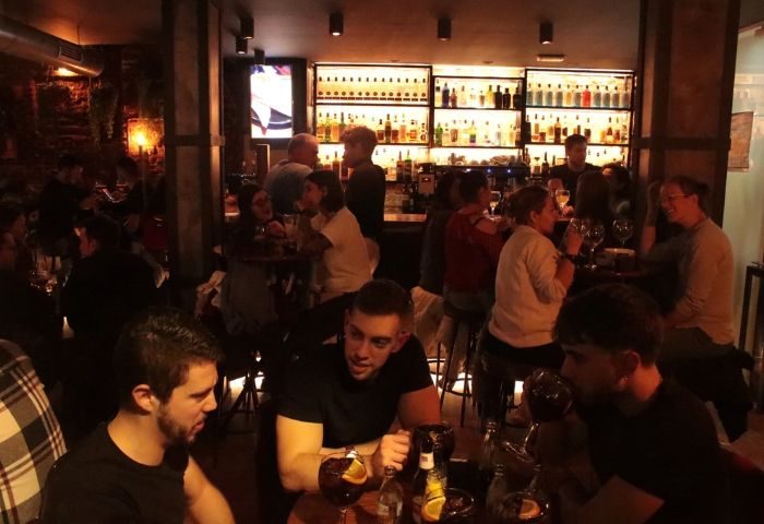 Madrid's Mystic Gay Bar: A lively scene with men & women enjoying drinks at tables and the bar. Bottles line shelves in the background.