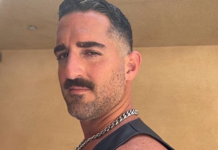 Daddy Big Hands by Roy: Close-up of a handsome, muscular gay man with a mustache, wearing a leather harness and chain. Gay travel.