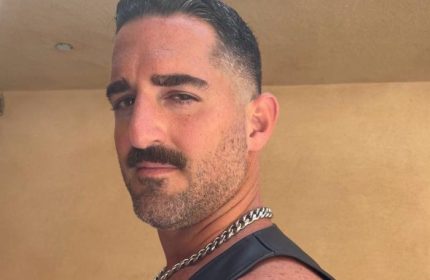 Daddy Big Hands by Roy: Close-up of a handsome, muscular gay man with a mustache, wearing a leather harness and chain. Gay travel.