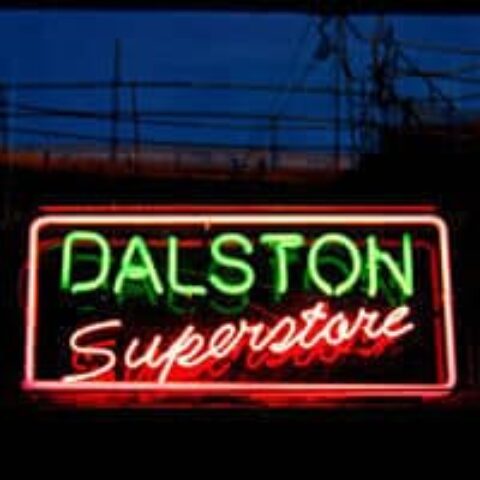 Neon sign for Dalston Superstore, a gay bar in London. Green and red lights illuminate the name against a dark background.