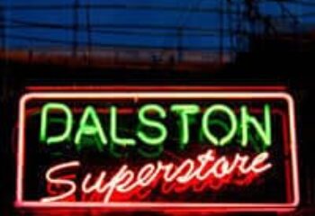 Neon sign for Dalston Superstore, a gay bar in London. Green and red lights illuminate the name against a dark background.