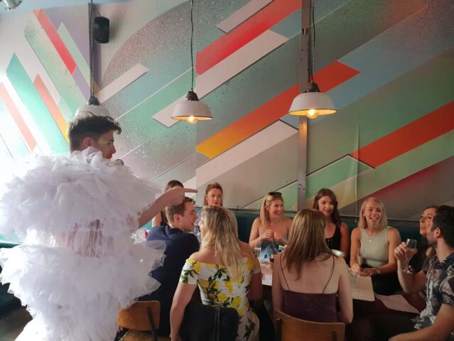 Drag queen performing at Dalston Superstore, a gay bar in London. Group of people sit at tables enjoying the show. Nightlife.