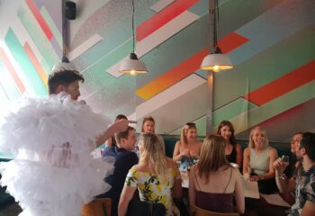 Drag queen performing at Dalston Superstore, a gay bar in London. Group of people sit at tables enjoying the show. Nightlife.