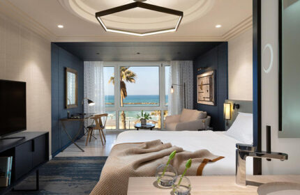 Dan Tel Aviv Hotel beachfront suite. Luxury gay honeymoon hotel with sea view. Modern room interior. Palm tree visible.
