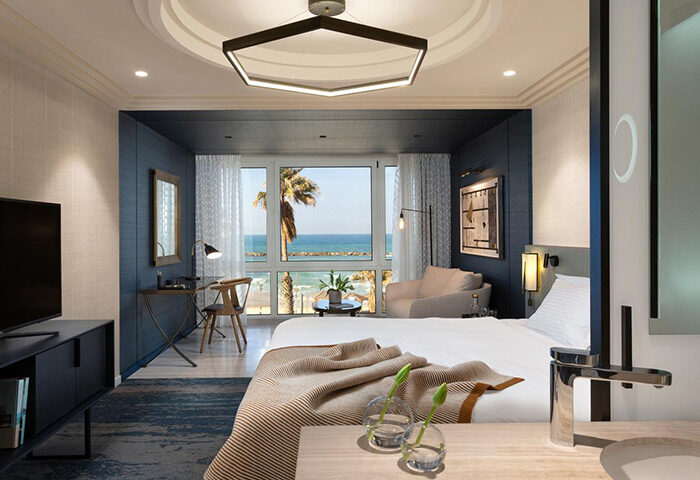Dan Tel Aviv Hotel beachfront suite. Luxury gay honeymoon hotel with sea view. Modern room interior. Palm tree visible.