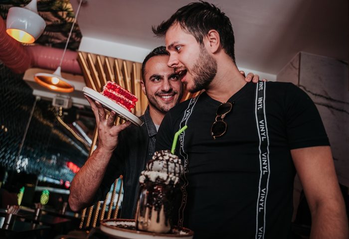 Two gay men at Del Sol Cafe. One holds cake, the other a milkshake. Gay travel advice, food, and fun.