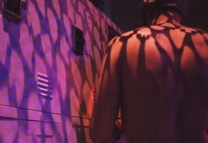Depot Milano gay travel: Shirtless man stands near a wall with purple lighting and shadow patterns. Gay nightlife in Milan, Italy.