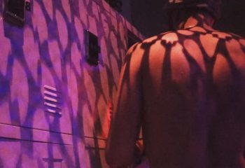 Depot Milano gay travel: Shirtless man stands near a wall with purple lighting and shadow patterns. Gay nightlife in Milan, Italy.